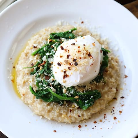 A close-up of savoury oatmeal garnished with spinach, and a runny poached egg, ready to eat.
