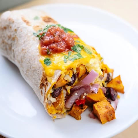 A close-up of a golden brown, fully-loaded Sweet Potato & Black Bean Breakfast Burrito on a plate.