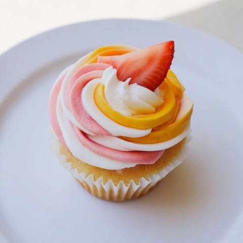 Fresh strawberry slices grace these Mango Strawberry Sunset Cupcakes, ideal for a summer celebration.