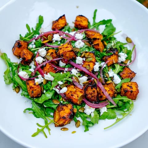 Colorful roasted sweet potato salad tossed in a zesty honey-lime dressing, featuring arugula, red onion, and feta cheese.
