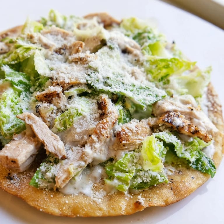A close-up of a savory Chicken Caesar Flatbread featuring chopped romaine, shaved parmesan, and grilled chicken on a golden, baked crust ready to serve.